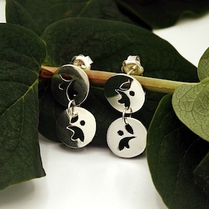 Peut inclure: Une paire de boucles d'oreilles pendantes en argent avec un délicat motif de feuilles. Les boucles d'oreilles sont suspendues à une branche feuillue verte.