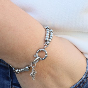 May include: A silver beaded bracelet with a silver clasp and a small silver cross charm.