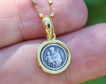 May include: A gold chain necklace with a round pendant featuring a silver image of Saint Anthony holding a baby.