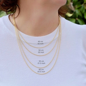 Puede incluir: Se muestran cuatro cadenas de oro de diferentes longitudes en una modelo que lleva una camisa blanca. Las cadenas están etiquetadas con sus longitudes en centímetros y pulgadas: 45 cm (18 pulgadas), 50 cm (20 pulgadas), 55 cm (21,5 pulgadas) y 60 cm (23,5 pulgadas).