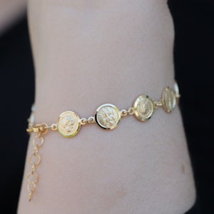 May include: A gold bracelet with a chain and round coin-shaped charms. The charms have a raised design.
