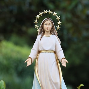 K&ouml;nnte beinhalten: Eine wei&szlig;e Statue der Jungfrau Maria mit einer goldenen Sternenkrone. Die Statue steht mit ausgestreckten Armen und tr&auml;gt ein wei&szlig;es Gewand mit einem goldenen G&uuml;rtel.