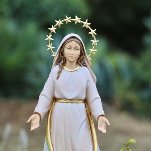 K&ouml;nnte beinhalten: Eine wei&szlig;e Statue der Jungfrau Maria mit einer goldenen Sternenkrone. Die Statue steht mit ausgestreckten Armen.