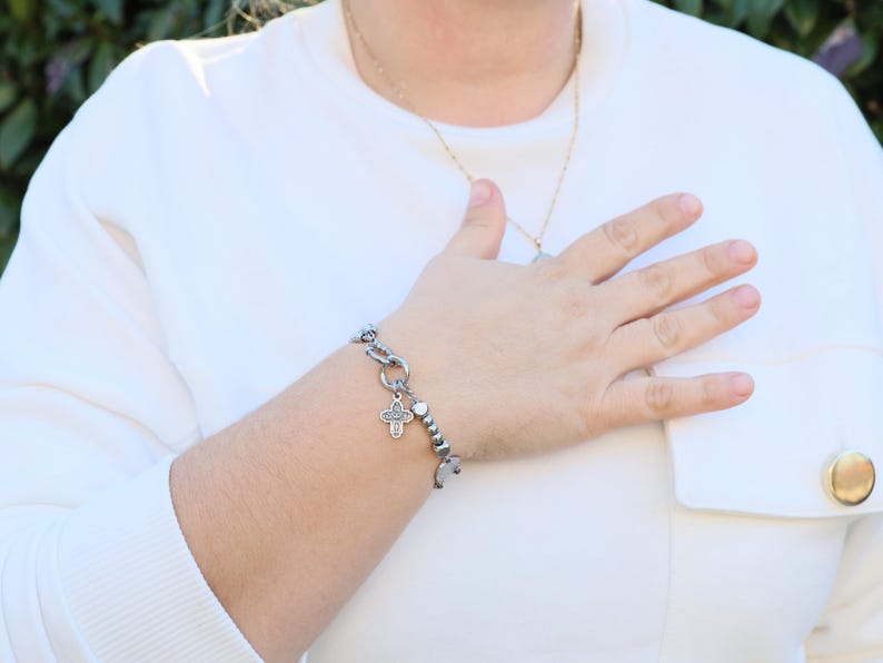 May include: A silver bracelet with a cross charm and small beads. The bracelet is on a person's wrist.
