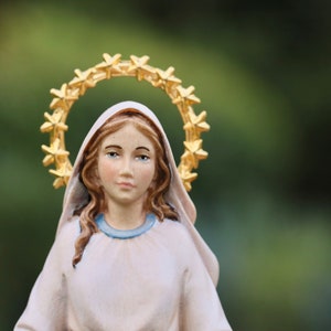 K&ouml;nnte beinhalten: Eine wei&szlig;e Figur einer Frau mit einem goldenen Sternenhalo. Sie tr&auml;gt ein wei&szlig;es Gewand mit einem blauen Kragen und hat lange braune Haare.