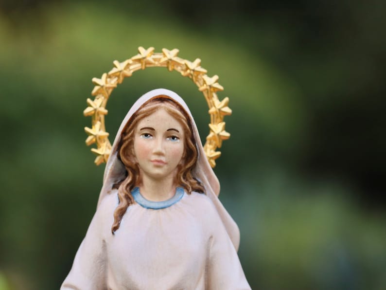 K&ouml;nnte beinhalten: Eine wei&szlig;e Figur einer Frau mit einem goldenen Sternenhalo. Sie tr&auml;gt ein wei&szlig;es Gewand mit einem blauen Kragen und hat lange braune Haare.
