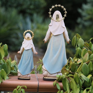 K&ouml;nnte beinhalten: Zwei blaue und wei&szlig;e religi&ouml;se Figuren der Jungfrau Maria, eine gr&ouml;&szlig;er als die andere, stehen R&uuml;cken an R&uuml;cken. Beide Figuren haben einen goldenen Heiligenschein mit Sternen um den Kopf.