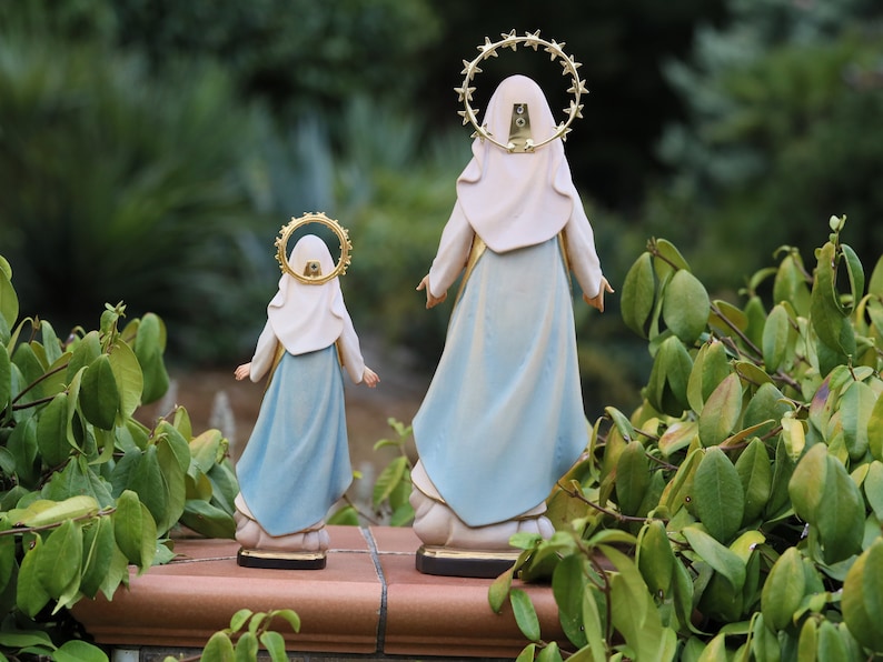 K&ouml;nnte beinhalten: Zwei blaue und wei&szlig;e religi&ouml;se Figuren der Jungfrau Maria, eine gr&ouml;&szlig;er als die andere, stehen R&uuml;cken an R&uuml;cken. Beide Figuren haben einen goldenen Heiligenschein mit Sternen um den Kopf.