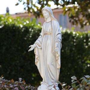 May include: White statue of the Virgin Mary with a gold trim on her robe. The statue is standing on a base with the word "Medjugorje" inscribed on it.