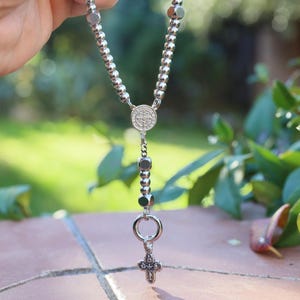 May include: A silver rosary with a round pendant and a small cross charm.