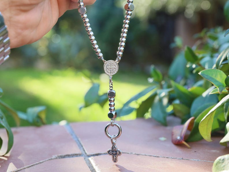 May include: A silver rosary with a round pendant and a small cross charm.