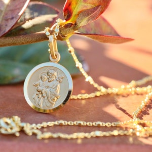 Pode incluir: Um colar de corrente de ouro com um pingente redondo que apresenta uma imagem detalhada de S&atilde;o Jos&eacute; segurando o menino Jesus. O pingente tem uma borda elevada e um acabamento liso e polido.