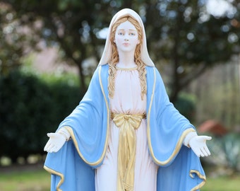 Könnte beinhalten: Eine weiße Statue der Jungfrau Maria mit langen blonden Haaren, die ein blaues Gewand mit goldenen Verzierungen und einem goldenen Gürtel trägt. Sie steht mit ausgestreckten Armen.