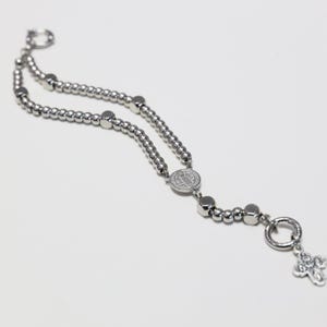 May include: A silver beaded bracelet with a silver charm featuring a cross and a round pendant with a religious image.