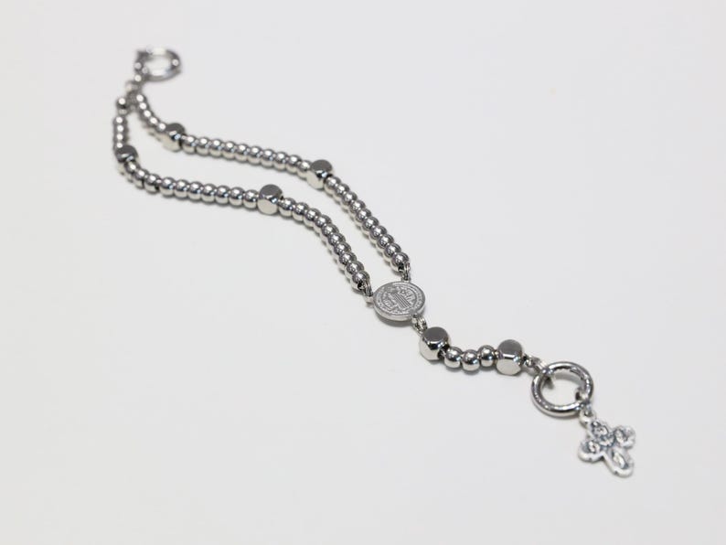 May include: A silver beaded bracelet with a silver charm featuring a cross and a round pendant with a religious image.