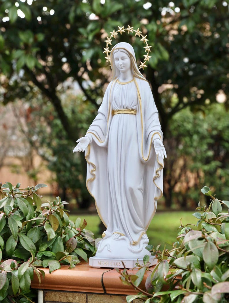 May include: White statue of the Virgin Mary with a gold star halo. The statue is standing on a base with the word "Medjugorje" inscribed on it.