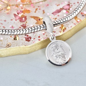 Könnte beinhalten: Silbernes Charm-Armband mit einem runden Anhänger, der ein detailliertes Bild der Jungfrau Maria mit einem Jesuskind zeigt. Der Anhänger ist an einer silbernen Kette befestigt.