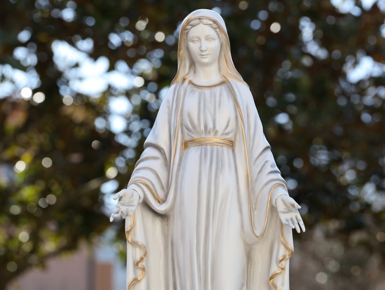 May include: White statue of the Virgin Mary with a gold trim on her robe and a soft, blurred background.