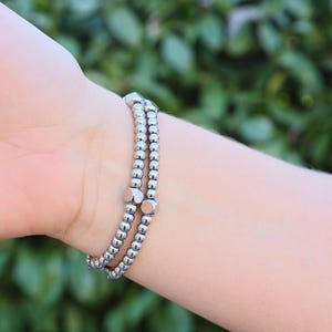 May include: A silver bracelet with multiple strands of small beads and larger, square-shaped beads.