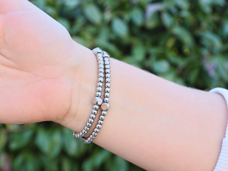 May include: A silver bracelet with multiple strands of small beads and larger, square-shaped beads.