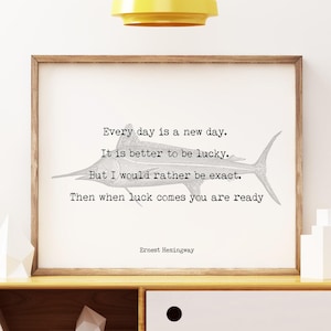 以下が含まれることがあります： アーネスト・ヘミングウェイの引用とカジキのイラストが描かれた額入りのプリント。プリントは、白い引き出しと上部に黄色のペンダントライトが付いた木製のキャビネットに表示されています。