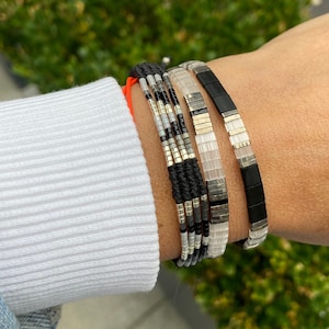 May include: A stack of bracelets with black, white, and silver beads. The bracelets are layered on a person's wrist.