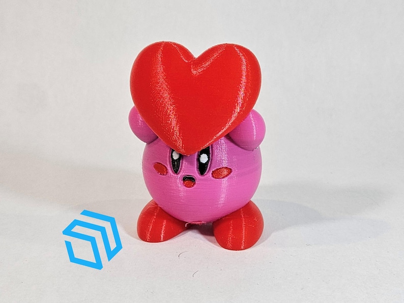 Pode incluir: Uma figura impressa em 3D rosa e vermelha de um personagem segurando um cora&ccedil;&atilde;o. O personagem tem um corpo redondo, bra&ccedil;os e pernas pequenos e um rosto bonito.