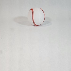 Pode incluir: Uma bola de beisebol branca com costuras vermelhas.