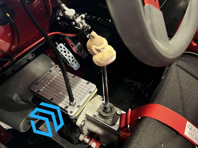 Pode incluir: Um close-up do interior de um carro com um c&acirc;mbio personalizado com uma cabe&ccedil;a de macaco marrom. O c&acirc;mbio est&aacute; preso a uma caixa de c&acirc;mbio de metal prateado. O interior do carro &eacute; preto com detalhes vermelhos.