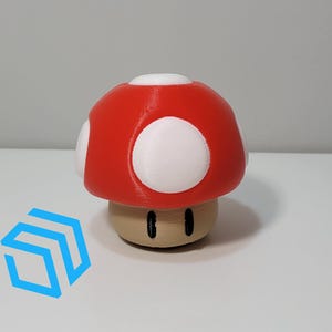 Pode incluir: Um cogumelo vermelho e branco impresso em 3D com um caule marrom e olhos pretos. O cogumelo &eacute; um personagem popular de videogame.