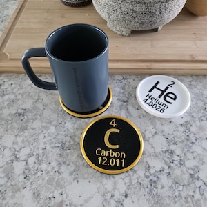 May include: A white ceramic mug with a black handle and the text "But First, Coffee" in a black, bold font. The mug is on a white surface.