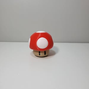 Pode incluir: Uma figurinha de cogumelo vermelho e branco com um caule castanho. O cogumelo tem manchas brancas no topo.