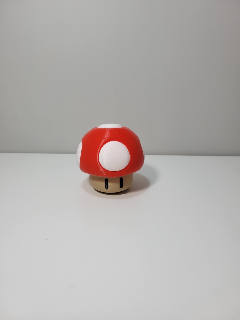 Pode incluir: Uma figurinha de cogumelo vermelho e branco com um caule castanho. O cogumelo tem manchas brancas no topo.
