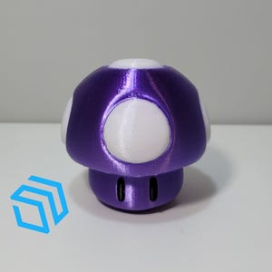Pode incluir: Um brinquedo em forma de cogumelo roxo e branco. O cogumelo tem um acabamento roxo met&aacute;lico brilhante e manchas brancas.
