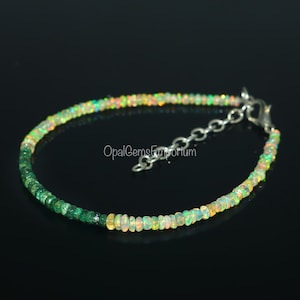 May include: A silver chain bracelet with green and white opal beads. The bracelet has a clasp closure. "OpalGemsEmporium" is printed on the background.