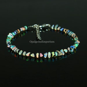 May include: A delicate bracelet made with a mix of iridescent opal and black onyx beads. The bracelet is strung on black thread and has a silver clasp. The bracelet is called "OpalgemsEmporium".
