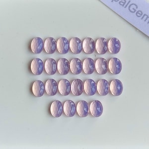May include: A collection of twenty-five small, oval-shaped, faceted lavender gemstones arranged in four rows. Each stone features a uniform cut with multiple reflective surfaces, displaying a consistent light purple hue throughout the set.