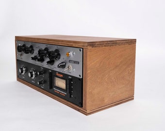 May include: A black and silver audio mixing amplifier with a wooden case. The front panel features knobs, switches, and a meter. The text "WARM AUDIO" is printed on the front panel.