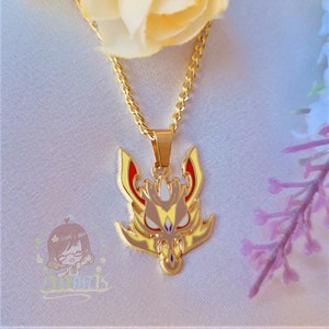 Peut inclure: Collier en chaîne dorée avec un pendentif en émail jaune, rouge et blanc représentant une tête de dragon stylisée.