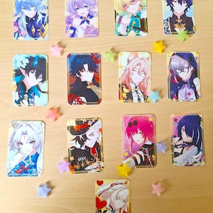 May include: A collection of rectangular anime-style character cards featuring various characters with colorful hair and outfits. The cards are decorated with star-shaped confetti in pastel colors, creating a playful and vibrant aesthetic.