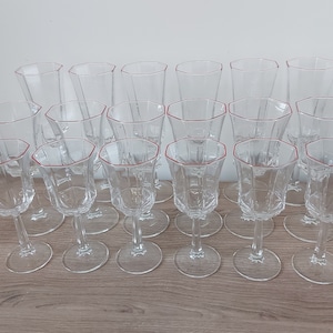 Peut inclure: Un ensemble de verres à pied en verre transparent avec un bord rouge. Les verres sont disposés sur une surface en bois. L'ensemble comprend différentes tailles de verres, dont des verres à vin et des verres à eau plus hauts.