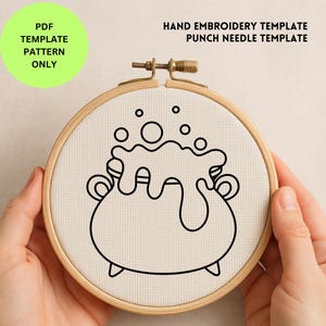 May include: A black line drawing of a bubbling cauldron is centered on a cream-colored fabric, held within a wooden embroidery hoop. The text "PDF TEMPLATE PATTERN ONLY" is in a green circle. Above the hoop, the text reads "HAND EMBROIDERY TEMPLATE PUNCH NEEDLE TEMPLATE."