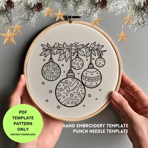 Op de afbeelding: Een handborduursjabloon in een houten hoepel toont een zwart-wit ontwerp van kerstballen die aan een tak hangen. De tekst "PDF TEMPLATE PATTERN ONLY INSTANT DOWNLOAD" is zichtbaar. Het ontwerp bevat sterren en decoratieve elementen.