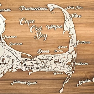 May include: A wooden cutting board with a laser-etched map of Cape Cod, Massachusetts. The map includes the towns of Provincetown, Wellfleet, Chatham, Falmouth, and Sandwich. The board is a light brown color with a natural wood grain.