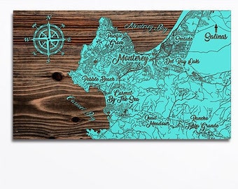 May include: A turquoise blue map of Monterey Bay, California, with the names of nearby towns and cities printed in black. The map is printed on a wood background.