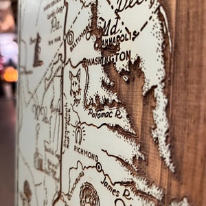 May include: A detailed map of the Mid-Atlantic region, including Maryland, Virginia, and surrounding areas, is etched into a wooden surface. Major cities like Washington, D.C., and Richmond are labeled. The map features intricate details of rivers and geographical features.