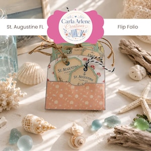 May include: A paper flip folio featuring a peach-coloured pocket with a white seashell pattern. Inside the pocket are several cream-coloured tags with the text St. Augustine Florida and an anchor icon, tied with brown twine and black and white string.