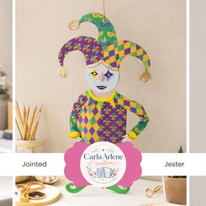 May include: A colorful, jointed jester decoration with a harlequin pattern in purple, yellow, and green. The jester has a white face with painted features and a decorative collar. The jester's hat has gold accents and is suspended by a string.