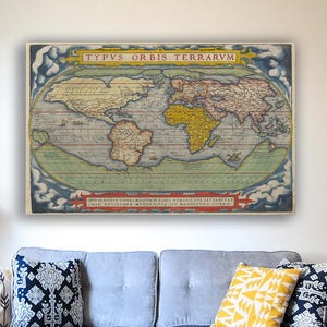 May include: A framed vintage world map print. The map, titled "TYPVS ORBIS TERRARVM", features continents in shades of yellow, brown, and green, set against a blue and white background. The frame is a light color, and the print is displayed above a sofa.