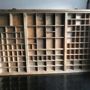 Könnte beinhalten: Ein Vintage-Druckertablett aus Holz mit mehreren Fächern unterschiedlicher Größe. Das Tablett besteht aus hellbraunem Holz und hat eine rechteckige Form. Es dient zur Organisation kleiner Gegenstände oder zur Präsentation von Sammlerstücken. Das Tablett ist wahrscheinlich ein Antiquität.